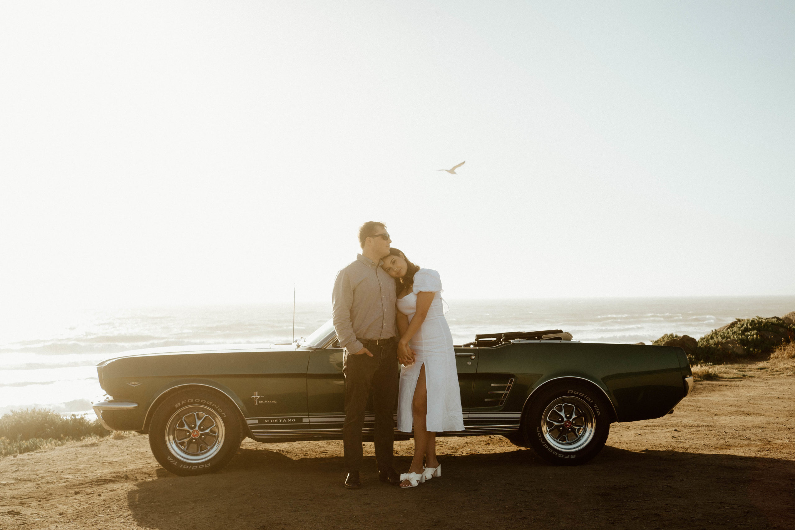 Engaged couple standing in front of vintage car for photos