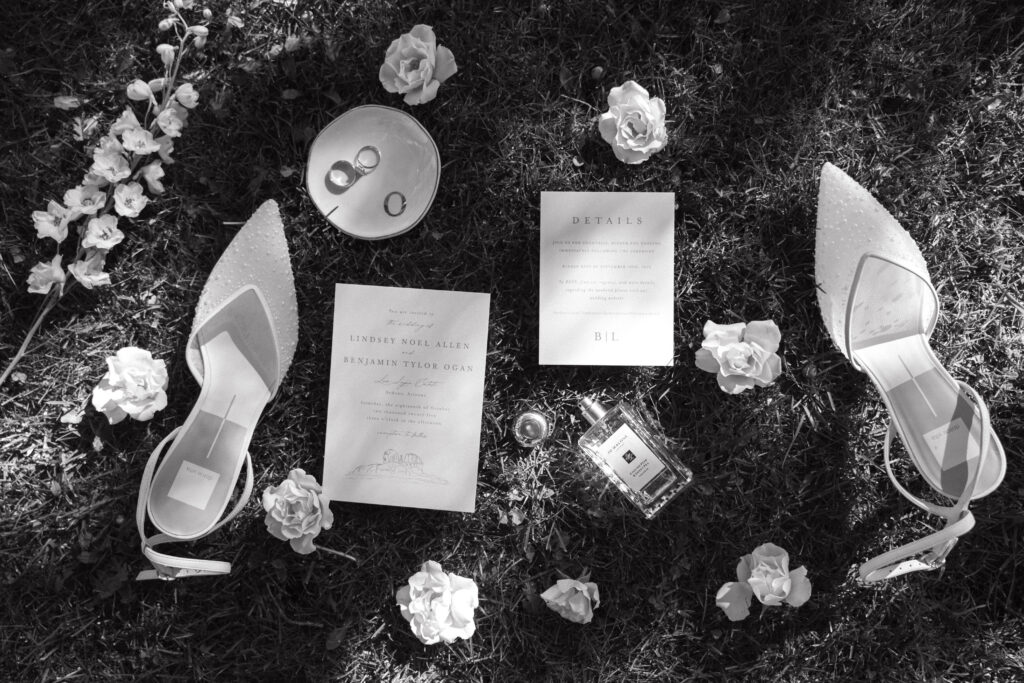 Wedding invitation, shoes and perfume on grassy area for wedding detail shots